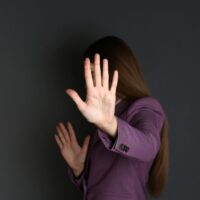 Woman showing stop gesture on dark background. Problem of sexual harassment at work