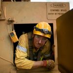 Male rope access technician maintenance worker wearing safety harness, helmet clear glass egress from confined space entry and exit manhole door door construction site