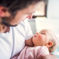 Unrecognizable father holding a sleeping toddler girl at home. Paternity leave.