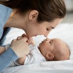 Happy Motherhood. Young mother playing with her adorable newborn baby at home, touching noses and smiling, loving millennial mom enjoying to spend time with her infant child, closeup Happy Motherhood. Young mother playing with her adorable newborn baby at home, touching noses and smiling, loving millennial mom enjoying to spend time with her infant child, closeup