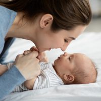 Happy Motherhood. Young mother playing with her adorable newborn baby at home, touching noses and smiling, loving millennial mom enjoying to spend time with her infant child, closeup Happy Motherhood. Young mother playing with her adorable newborn baby at home, touching noses and smiling, loving millennial mom enjoying to spend time with her infant child, closeup
